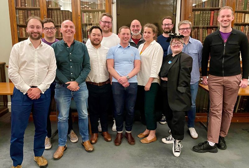 12 members of the 2022/23 Sedos Trustees and Management Committee.standing in a line in front of a wall of bookcases. They are all smiling. 